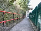Railway station pathway, fitted with red DDA disability handrails. Featuring a green safety fence to the right