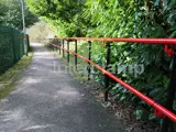 Railway station walkway with DDA disability handrails, powder coated in red and black. Green fence to the left hand side