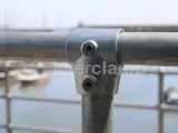 up close picture of a key clamp link onto a hand railing system over looking a marina with boats in