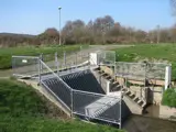 mesh handrails fitted over river dam and stairway for pedestrian safety. Surrounded by grass 